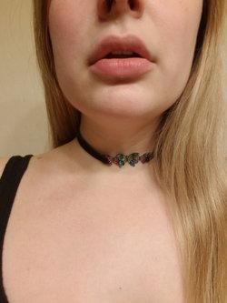 Close-up of a blonde woman wearing a black choker with colorful butterfly charms, showing her neck and collarbone in a