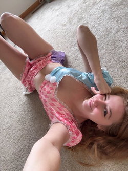 Woman in pink and blue checkered lingerie lies on carpet, smiling at the camera.