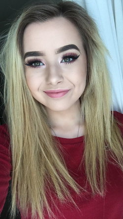 Blonde woman with long hair wearing a red top and makeup.