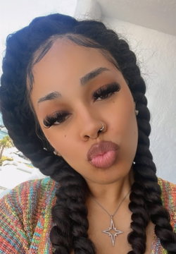 Woman with long dark braids, wearing colorful top and star pendant, making a playful face in a selfie.