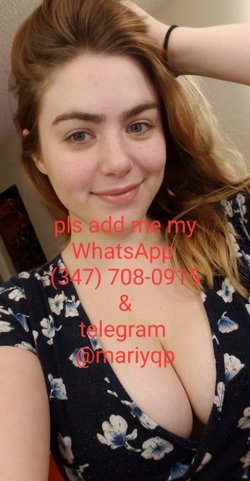 A woman with light brown hair and green eyes smiles softly in a selfie, wearing a dark floral top with a deep neckline