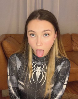 A young woman with long ombre hair and blue eyes sticks her tongue out while wearing a black and white Spider-Man