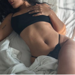A person with a curvy body type lies on their side in a black bra and white sheets.