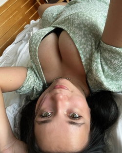 A woman with dark hair and green eyes lies on her back, wearing a light green patterned top, looking up at the camera