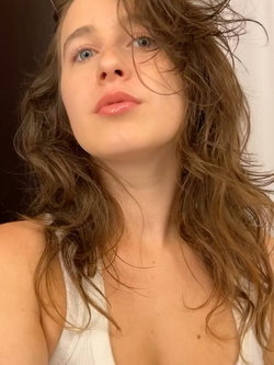 A young woman with long, wavy brown hair and a white top.