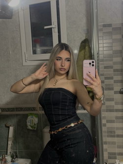 Slim curvy blonde takes a selfie in bathroom wearing strapless denim top and jeans.