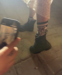 Person in black boots and patterned socks standing on tiled floor.