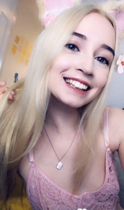 Blonde woman in pink lace top and bunny ears smiles at the camera in a cozy room.