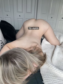 A blonde woman lies face down on a bed in a bedroom with white doors behind her.
