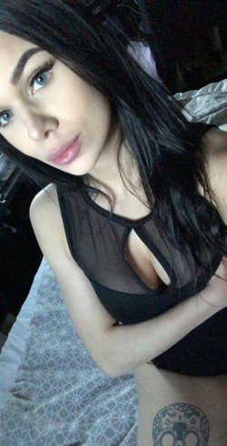 Woman with long dark hair in a sheer black top on a patterned bed.