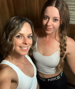 Two women in white tops smile for a selfie in a dimly lit room.