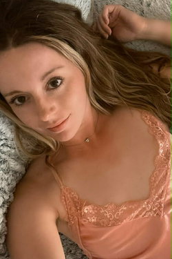 Woman with long hair in a pink lace bralette lying on a bed.