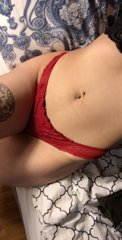 Person in red lingerie lying on patterned sheets with a visible tattoo.