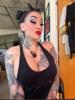 A person with tattoos and makeup poses in a black top.