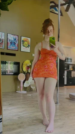 Redhead woman in a red dress taking a selfie in a dance studio.