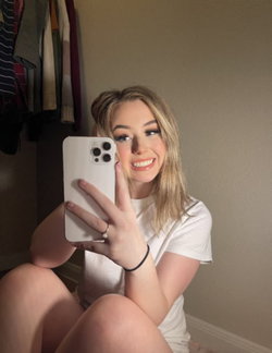 Blonde woman in white top taking a selfie in a bedroom.
