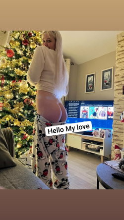 Slim blonde woman in white top and pulled-down Mickey Mouse pants stands in a Christmas-decorated room.
