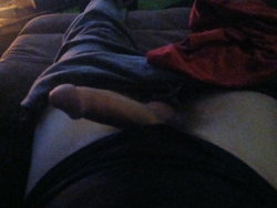A person lies on a couch, partially covered by a dark blanket, with bare feet visible and a red garment nearby.
