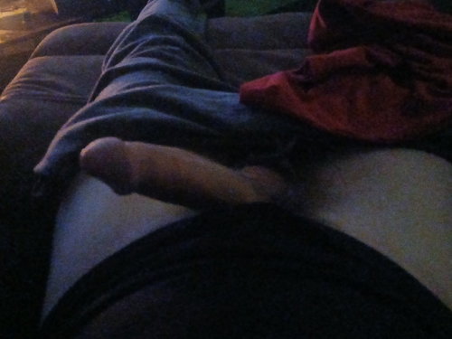 A person lies on a couch, partially covered by a dark blanket, with bare feet visible and a red garment nearby.