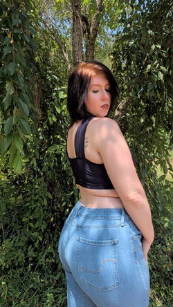 Woman with short dark hair in a black crop top and light jeans stands outdoors.