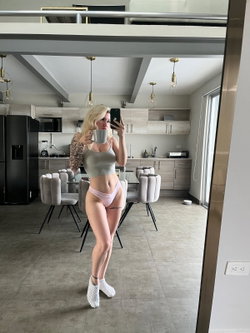 Tattooed blonde taking a selfie in a modern kitchen while wearing a crop top and pink underwear.