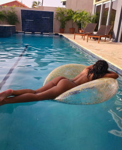 Curvy woman with dark curly hair lounging on a glittery float in a pool, wearing a thong bikini bottom.