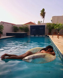 Curvy woman with dark hair relaxing on a glittery float in a pool, wearing a bikini bottom, surrounded by palm trees