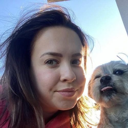 Selfie of a brunette woman wearing a red top posing with a small dog outdoors.