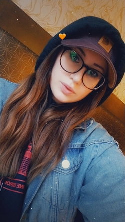 Woman with long brown hair, glasses, and a beanie sits indoors