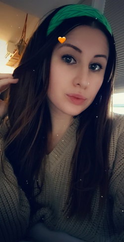 A brunette woman with a green headband and heart stickers poses in a selfie.