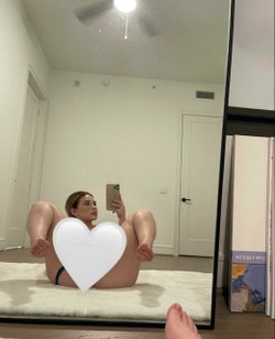Woman with a heart-shaped light prop sits on a bed in a minimalist room.