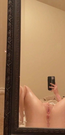 A person in a beige thong takes a selfie in a mirror.