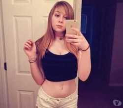 Redhead woman in a black crop top and white shorts taking a selfie in a mirror.