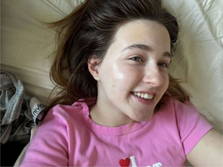 A young woman with brunette hair in a ponytail, wearing a pink t-shirt, lying on a couch.