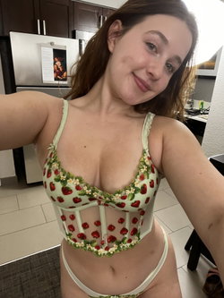 Woman in a strawberry-patterned corset posing in a kitchen.