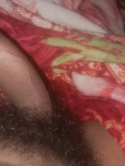 Close-up of a person's pubic area with dark curly hair, partially covered by a red and green patterned blanket.