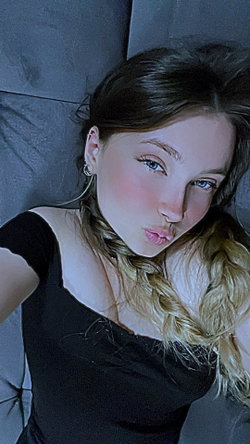 A woman with dark hair and a black top poses in a dimly lit room.