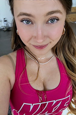 A woman with long brown hair and a pink sports bra smiles at the camera.