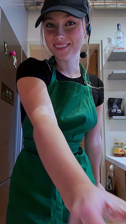 Woman in green dress and black cap smiling in a kitchen.