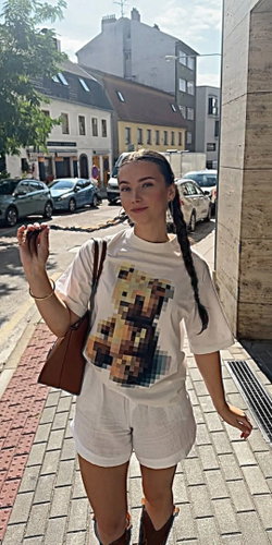 Woman with long braids in a white outfit poses on a city street.