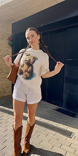 Woman with braided hair in white outfit and cowboy boots standing on a sidewalk.
