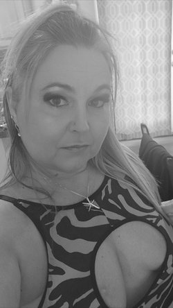 Blonde woman with nose piercing and heavy makeup in zebra-print top with cutouts exposing breasts, indoor selfie.