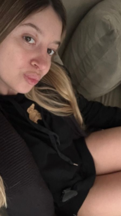 A woman with highlighted hair lies on a couch, wearing a black hoodie, making a playful face toward the camera.