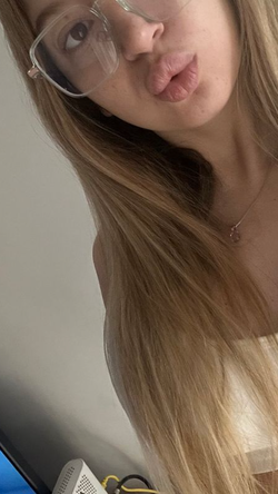 Slim blonde woman with glasses and long hair puckers her lips in a selfie.