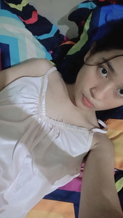 A person with dark hair in a white top lies on a colorful bed.