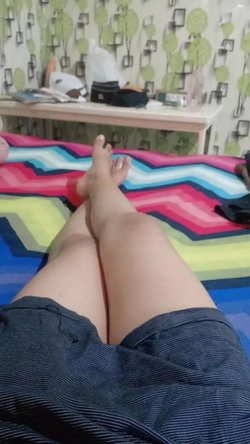 Bare legs and red-painted toes extended toward camera on colorful bed, wearing dark gray shorts.