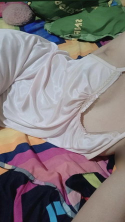 Slim woman in white satin slip on colorful messy bed, side profile with slipped strap.