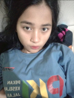 Slim Asian woman with long black hair pouts in blue graphic t-shirt, lying on bed.
