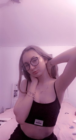 A woman with glasses and a black top poses in a pink-lit room.