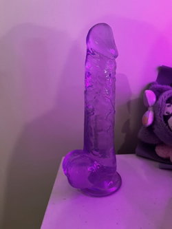 A large purple dildo on a white surface with a plush toy in the background.